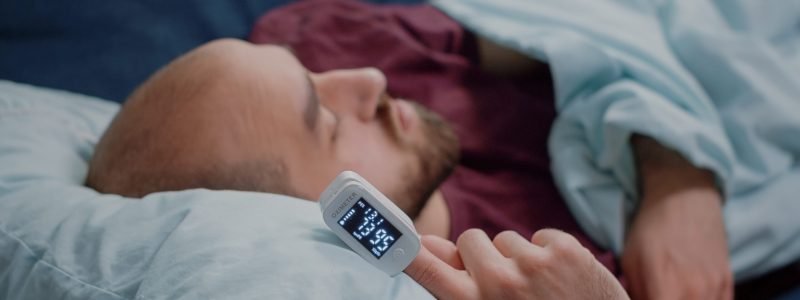 Close up of oximeter on hand of ill person resting while measuring oxygen saturation and pulse pressure to check virus symptoms. Sick adult using device for healthcare treatment